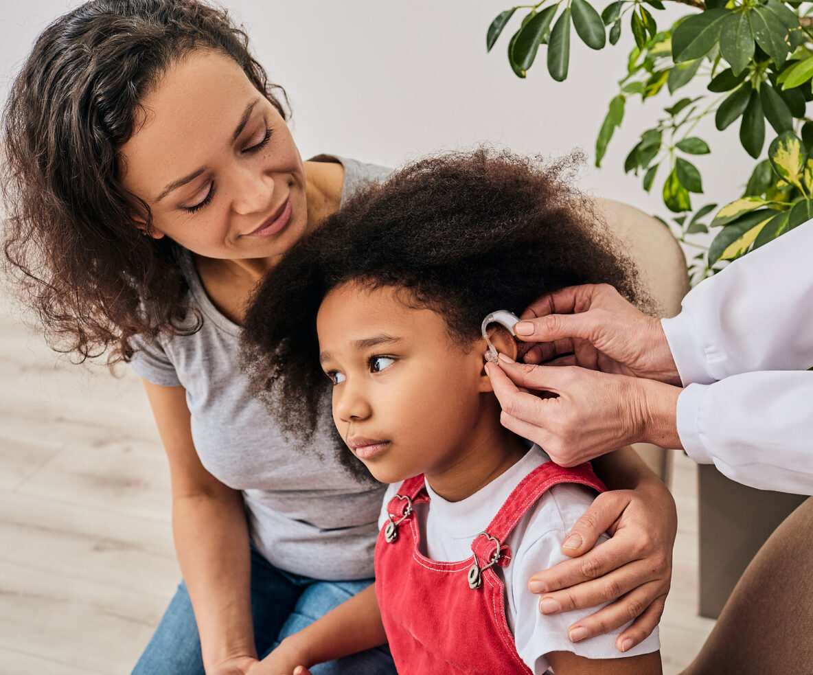 Cute girl with her mother during install hearing aid by her audiologist. Hearing treatment for a child