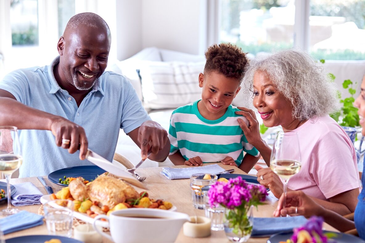 Grandfather Carving As Multi Generation Family Sit Around Table